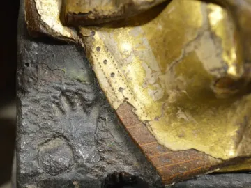 Close-up of a burnt hand imprint on the Fisenne Altarpiece, showing dark carved wood and worn gold leaf.