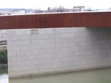 Hombre Río statue partly submerged in water beside a bridge pier, with a bird perched on its head.