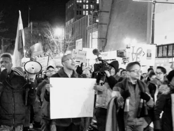 A white LOVE sign with a tilted O held above a crowd at a nighttime protest.