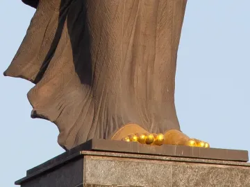 Lower part of the Statue of Sofia showing bare feet and draped stone folds on a dark pedestal.