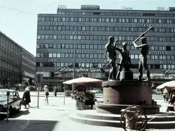 The Three Smiths bronze monument showing three men hammering an anvil on a stone base in a city square.