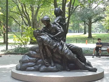 Vietnam Women\'s Memorial bronze sculpture showing three figures on a circular base in a leafy park setting.
