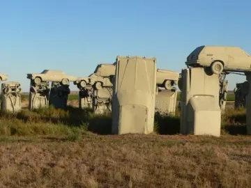 Carhenge sculpture made of tan-colored cars standing in a dry grassy field under a clear blue sky.