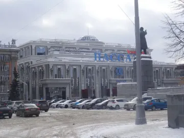 Lenin Monument on a snowy stone pedestal beside a light pole, with an ornate building in the background.