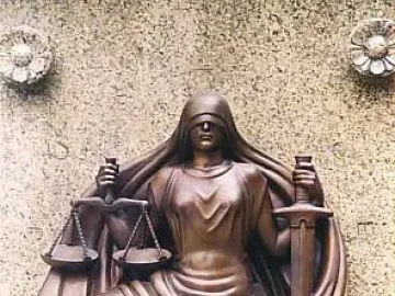 Bronze relief sculpture of Lady Justice holding scales and a sword against a stone wall.