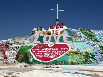 Salvation Mountain with a white cross on top, covered in colorful painted religious messages and symbols.
