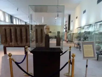 The Warka Mask displayed in a glass case on a dark pedestal in a museum hall.