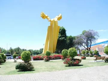 Ángel Custodio sculpture with bright yellow abstract forms in a landscaped park.