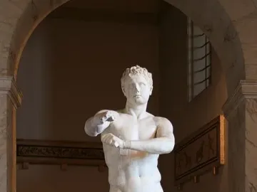 Apoxyomenos, a white marble nude male statue, shown under a museum archway scraping his left forearm.