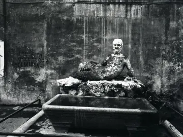 Babuino Fountain with a weathered reclining bearded stone statue above a small basin.