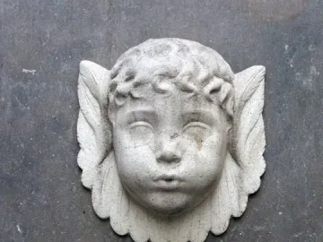 Font de Santa Eulàlia: a weathered stone cherub head above a brass water spigot on a dark wall.