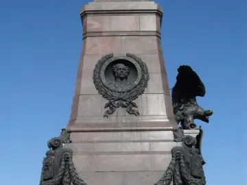 Lower section of the Monument of Alexander III with a bronze bust relief, draped garland, and a winged eagle on a granite pedestal.