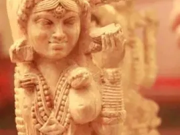 Pompeii Lakshmi ivory figurine shown on a clear stand with its reflection visible in a mirror behind it.