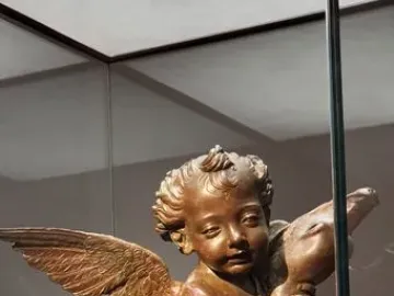 Bronze Putto with a Dolphin sculpture displayed on a white plinth in a glass case.