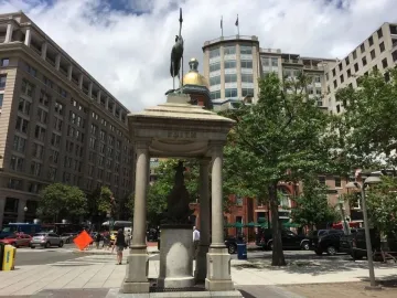 Temperance Fountain, a stone pavilion topped with a crane statue on a busy city sidewalk.