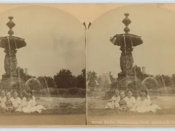 Children seated on the grass in front of the Bartholdi Fountain with water flowing into a surrounding pool.