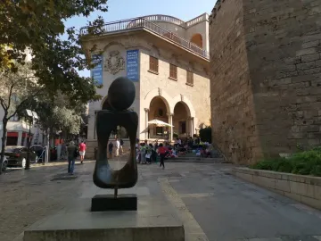 Monument a la dona bronze sculpture with a dark oval sphere balanced on an abstract hollow form outdoors.