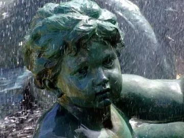 Bronze child statue from the Monument aux Girondins fountain covered in flowing water.