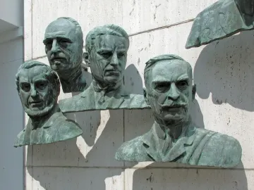 Four bronze busts from the Polio Hall of Fame mounted on a light stone wall, with part of a fifth bust visible.