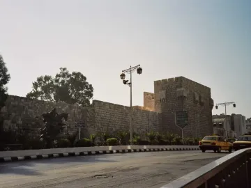 An equestrian statue of Saladin stands beside a massive stone wall with a road curving past it.