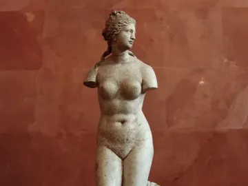 Venus Tauride marble statue with missing arms, standing beside a draped pillar.