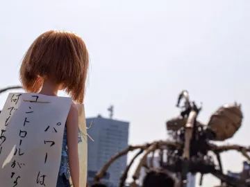 Doll with reddish-brown hair and a Japanese sign in front of La Princesse, with the large mechanical spider blurred in the background.