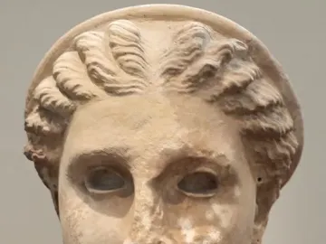 Weathered stone head of Lycosoura Artemis with hollow eyes, wavy hair, and a circular diadem.