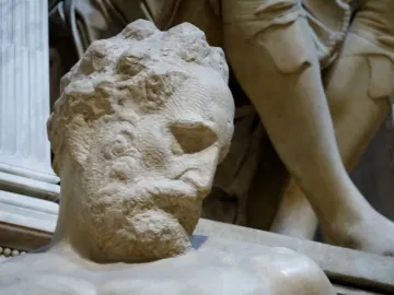 Close-up of Michelangelo’s Dusk showing a marble male figure with a tilted head, textured beard, and shadowed eyes.
