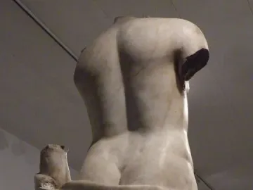 The Venus Unica sculpture shown from behind, a headless and armless stone figure with draped folds around the hips.
