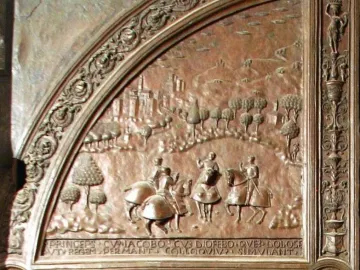 Close-up of a bronze gate relief showing horsemen in a historical landscape with Latin inscription and decorative scrollwork.
