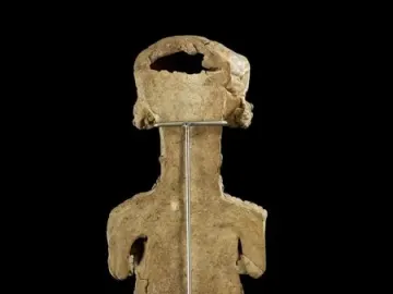 Back view of the Lady of Ibiza clay figure with a rough surface and a metal support rod.