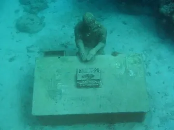 The Lost Correspondent underwater sculpture at Molinere Underwater Sculpture Park, showing a seated figure at a desk with a typewriter on the seabed.
