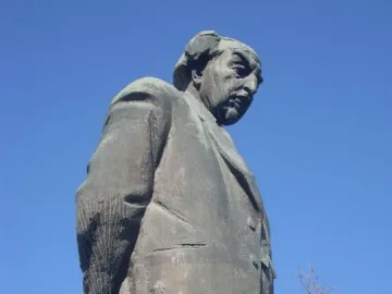 Monument to Avetik Isahakyan showing a dark statue of a man in a suit holding a cane against a blue sky.