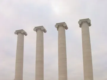 The Four Columns standing behind a fenced construction site under an overcast sky.