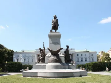 Tadeusz Kościuszko Monument with a bronze figure on a pedestal, flanked by additional sculptures including an eagle in a grassy park.