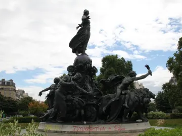 The Triumph of the Republic bronze monument with a central female figure standing on a globe, surrounded by dynamic figures and lions, on a stone base marked with red graffiti.