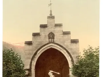 Winkelried Memorial with a stone arch niche framing a white marble sculpture of two figures, set among trees with mountains in the background.