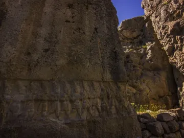Yazılıkaya rock reliefs carved along a large stone wall in a narrow passage with sky visible above.