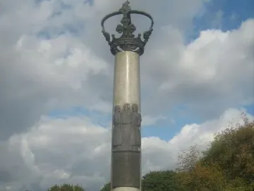 Electio Viritim Monument with a dark crown atop a light-colored shaft and relief figures on the central panel.