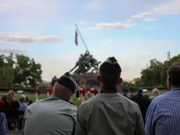 Marine Corps War Memorial with spectators seated in the foreground and the bronze flag-raising sculpture in the background.