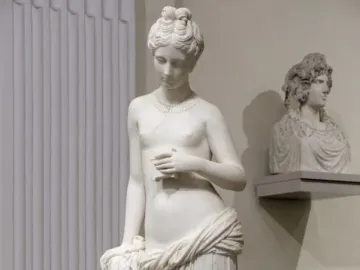 Pandora marble statue of a standing woman holding a small object, with drapery around her lower body.