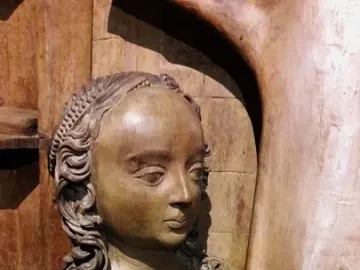 Wooden bust of Saint Luke with long curly hair and hands held out in front.