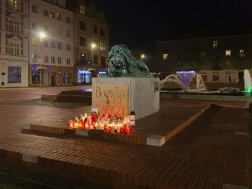 Sleeping Lion sculpture on a pedestal with candles and a sign arranged below it at night.