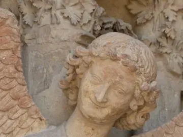 Smiling Angel sculpture with curly hair, a gentle smile, and raised arm on Reims Cathedral