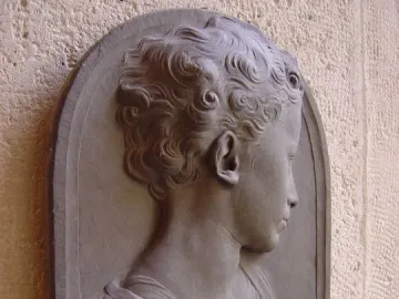 Bust of a child in gray stone relief, shown in profile with curly hair and draped clothing.