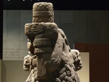 Left-side view of the Coatlicue stone sculpture, showing its carved skulls, necklace, and textured skirt-like body.