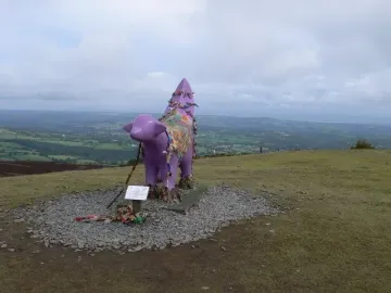 Superlambanana sculpture covered in colorful ribbons and fabric on a grassy hill
