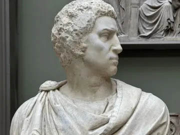 Marble bust of Brutus shown in sharp profile with curly hair and draped clothing.
