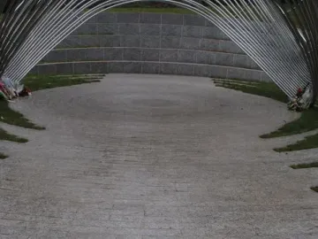 Infinite Wave memorial with arched metal bars forming a tunnel-like walkway beside a curved stone wall.