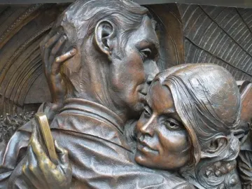 The Meeting Place bronze sculpture showing a man kissing a woman’s forehead in a close embrace.